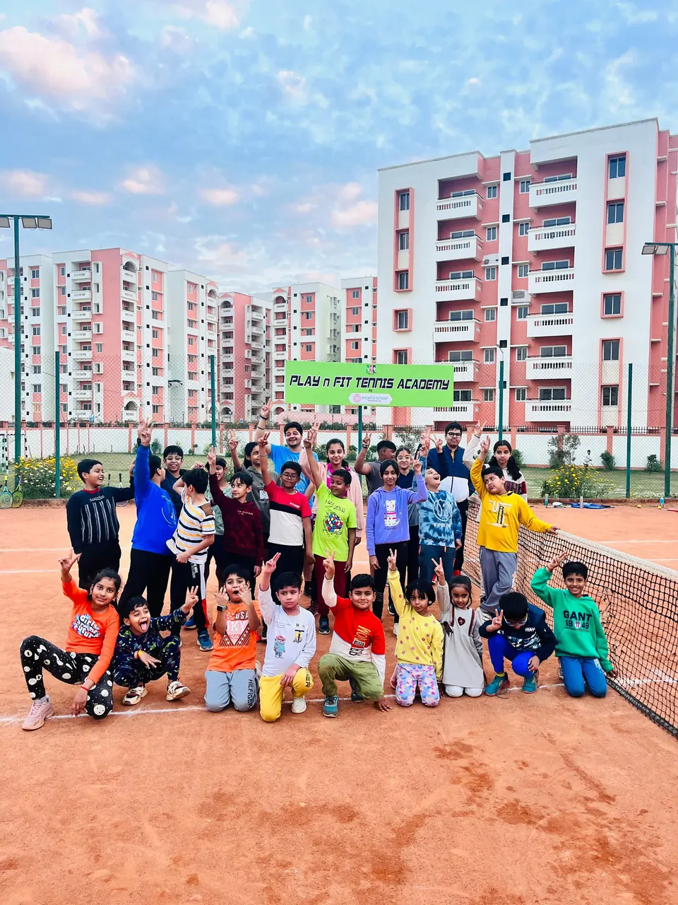 Juniors cheering together in front of the PLAY n FIT Tennis Academy sign