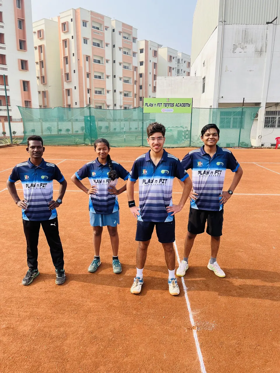Four PLAY n FIT players in academy kit standing on a clay court