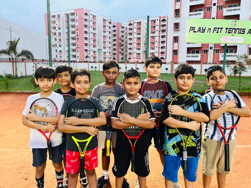 Juniors in front of the PLAY n FIT Tennis Academy sign on the clay courts