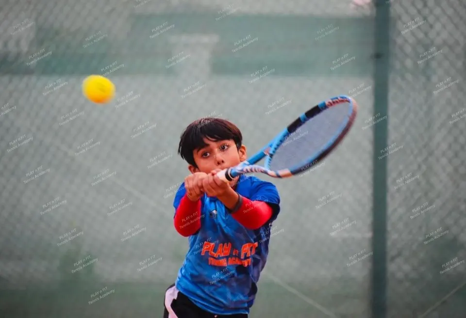 Young player in blue academy kit striking a two-handed backhand