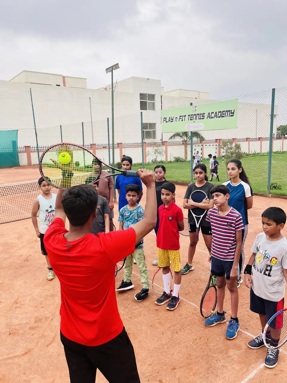 Coach demonstrating a stroke to a group of juniors on court