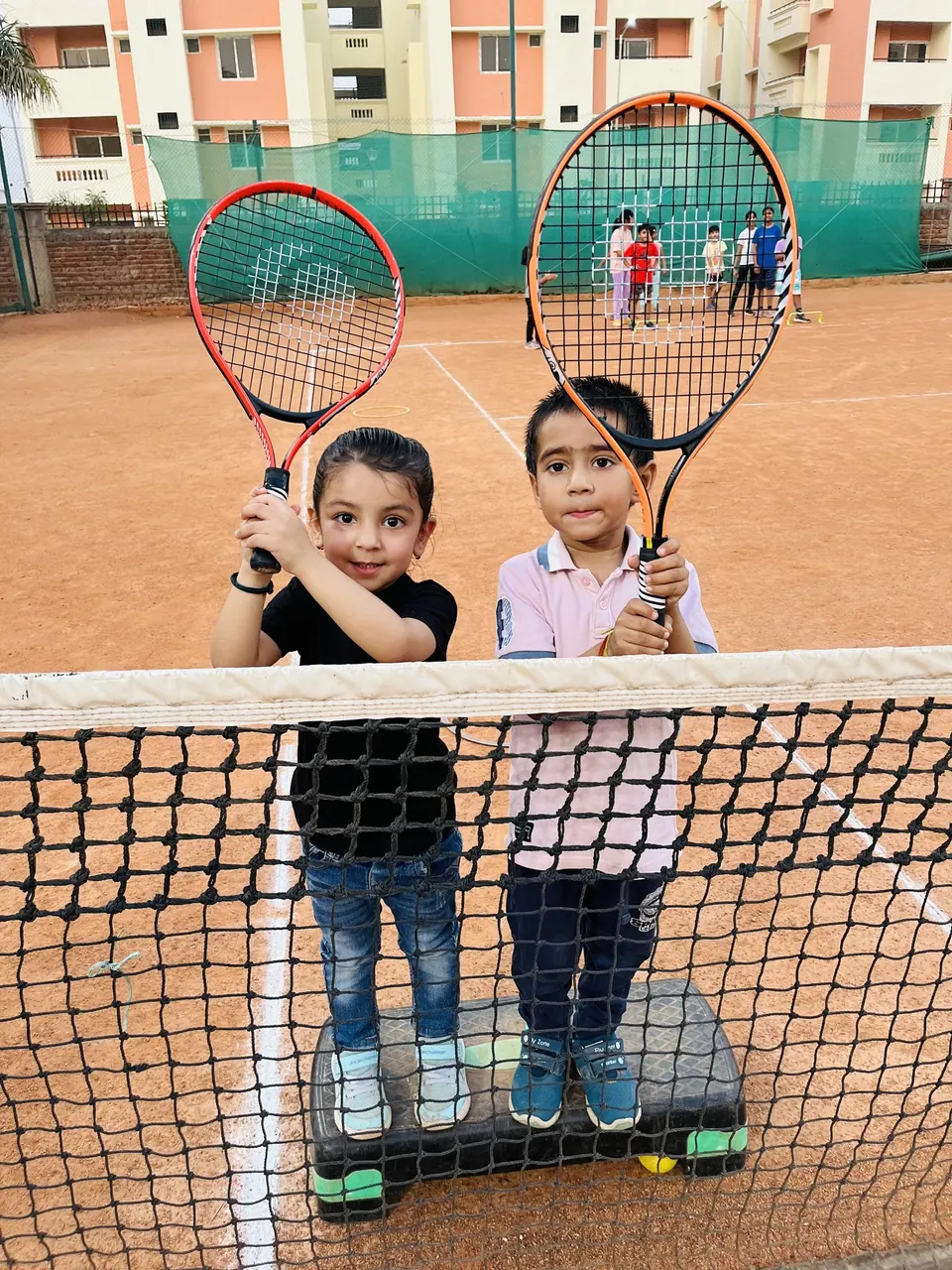Two young children holding up tennis racquets at the net